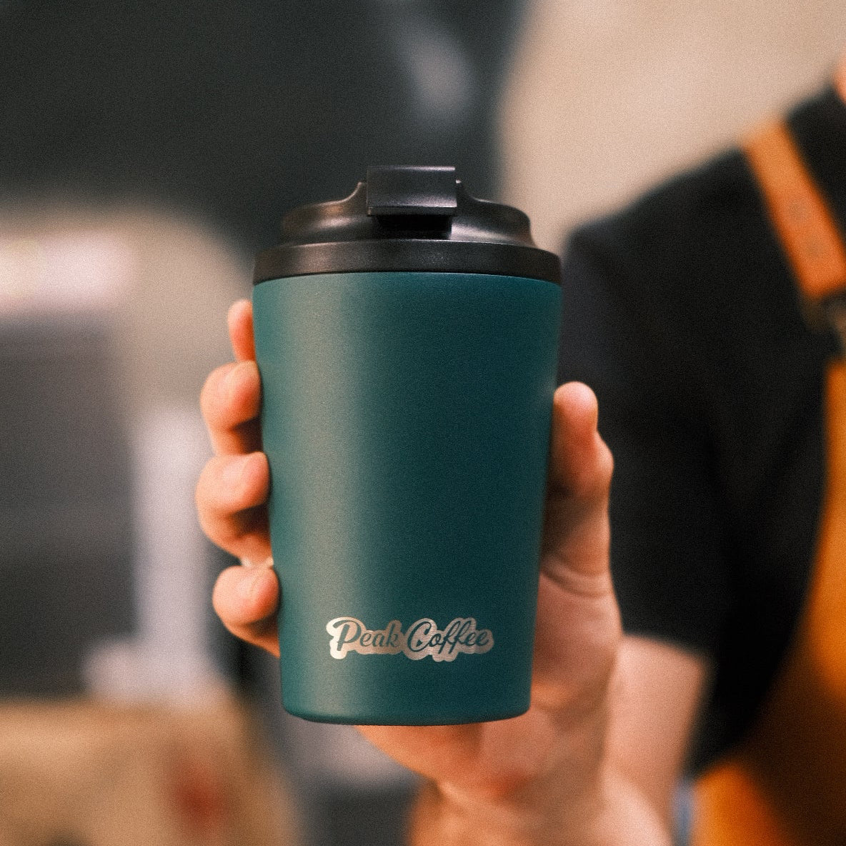 Hand holding a teal insulated mug with a blurred background