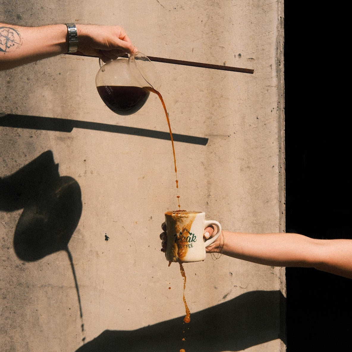 Person holding a cup of coffee with a spilled shot on a concrete surface
